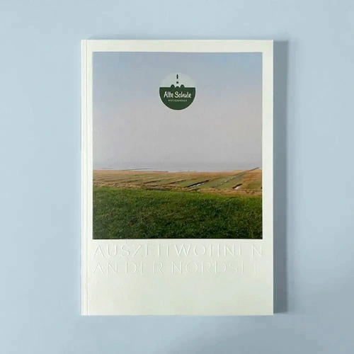 Broschüre der 'Alte Schule Westerhever' mit Titelbild einer nordfriesischen Landschaft und eingeprägtem Schriftzug 'Auszeitwohnen an der Nordsee'.