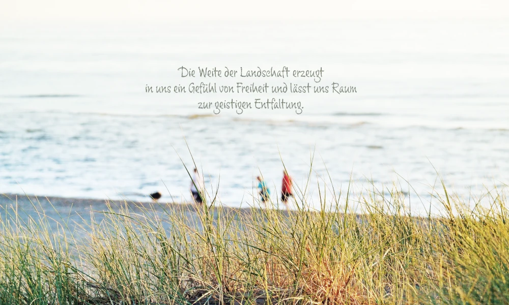 Blick durch Dünengras auf einen Strand mit drei Personen und dem Zitat 'Die Weite der Landschaft erzeugt in uns ein Gefühl von Freiheit und lässt uns Raum zur geistigen Entfaltung'.