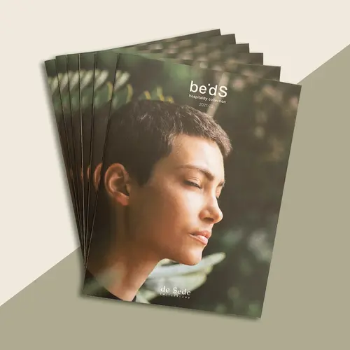 Mehrere Exemplare eines Katalogs mit dem Titel "be°DS hospitality collection 2021/22" von de Sede, auf dem Cover eine Frau mit kurzen Haaren und geschlossenen Augen vor natürlichem Hintergrund.
