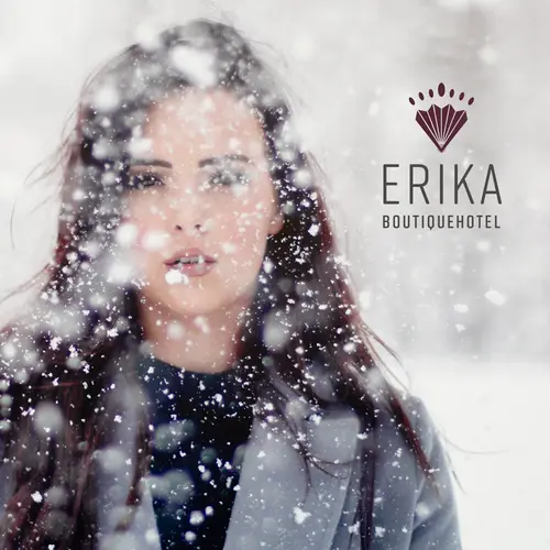 Junge Frau mit dunklen Haaren in winterlicher Szenerie, umgeben von fallendem Schnee, mit dem Logo und Schriftzug "ERIKA BOUTIQUEHOTEL" auf der rechten Seite.