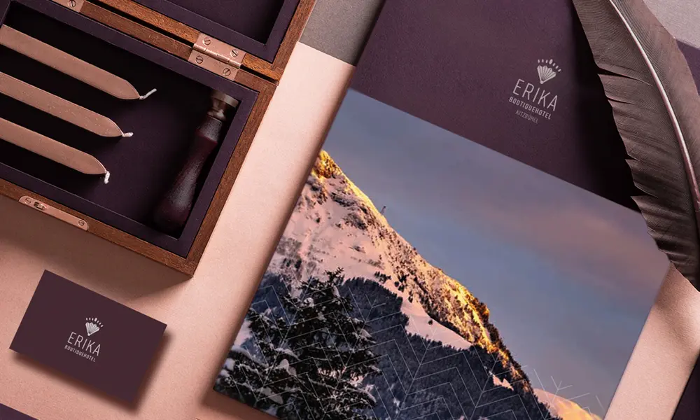 Flachliegende Darstellung mit Branding-Elementen des Erika Boutiquehotels, einschließlich einer Mappe mit Bergmotiv, einer Visitenkarte, Federn, Siegelwachs und einer Holzbox mit Kerzen.