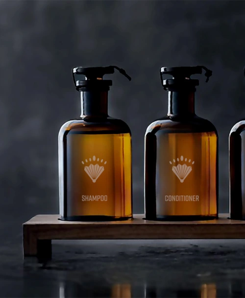 Nachfüllbare Braunglasflaschen für Shampoo und Conditioner mit eingraviertem Logo des Erika Boutiquehotels Kitzbühel, präsentiert auf einem Holzständer.