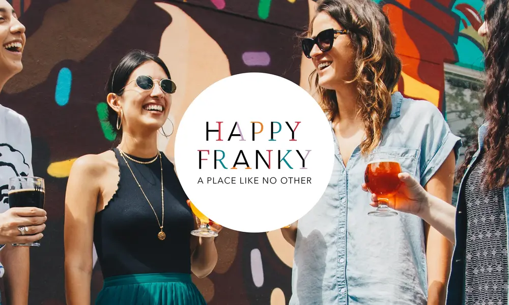 Gruppe lachender Menschen mit Getränken vor bunter Wand, zentriert das Logo von 'Happy Franky' mit dem Slogan 'A Place Like No Other'.