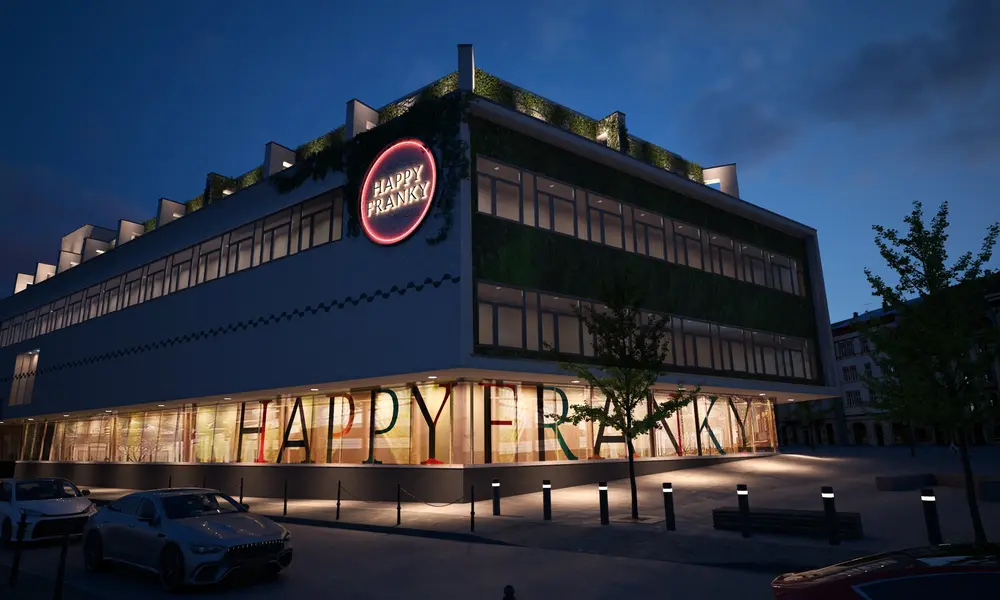 Gebäude 'Happy Franky' bei Nacht mit beleuchtetem Logo und Schriftzug, moderner Architektur und begrünten Fassaden.