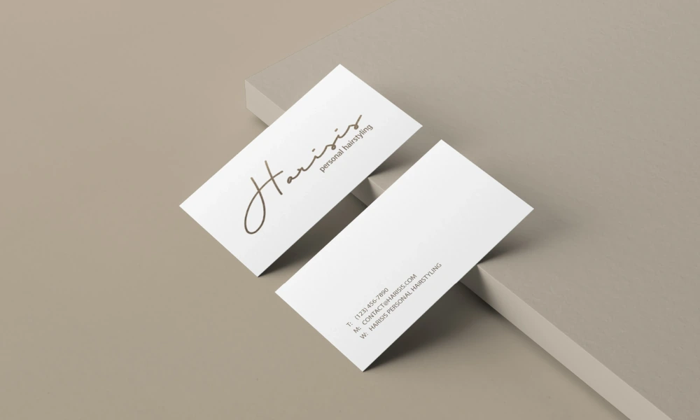 Zwei weiße Visitenkarten für „Harisis – Personal Hairstyling“ auf einer beige-braunen Oberfläche, eine mit Logo, die andere mit Kontaktdaten.