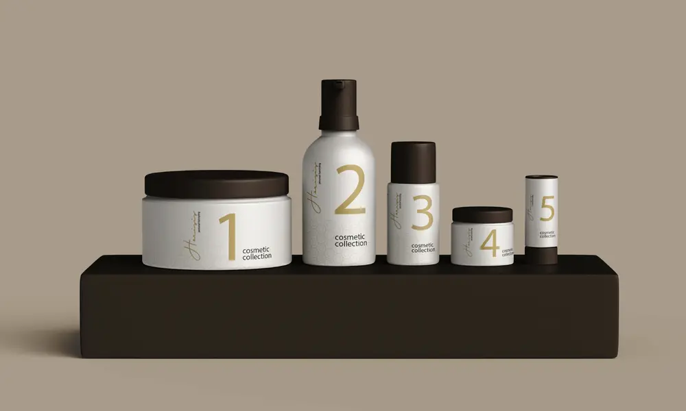 Fünf minimalistisch designte Kosmetikprodukte der „Harisis Cosmetic Collection“ mit nummerierten Etiketten, auf einem schwarzen Podest vor beigem Hintergrund.