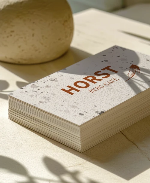 Stapel hochwertiger Visitenkarten mit dem Logo des HORST Berg Café auf strukturiertem Papier – natürliches Design in warmem Licht mit Schatteneffekten für ein stilvolles Markenbild.