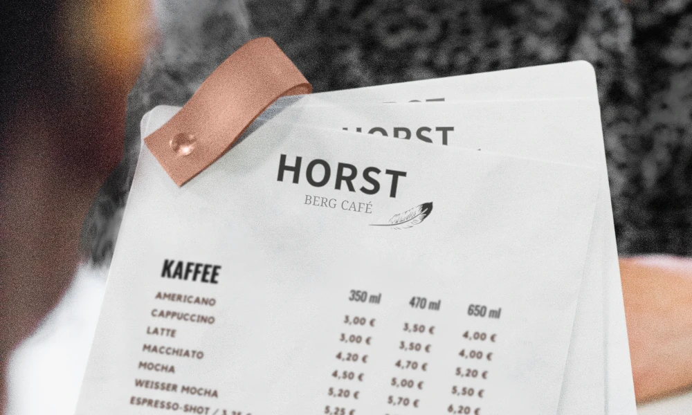 Gedruckte Getränkekarte des HORST Berg Café mit Lederclip – klares, modernes Design mit Fokus auf Kaffeespezialitäten in verschiedenen Größen und Preisen.        ChatGPT fragen