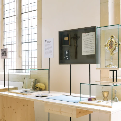 Heller, gotischer Kreuzgang mit hohen Spitzbögen, Ausstellungstafeln und Skulpturen, mit einem schwarzen Aufsteller mit der Aufschrift "DOMKAMMER" im Vordergrund.