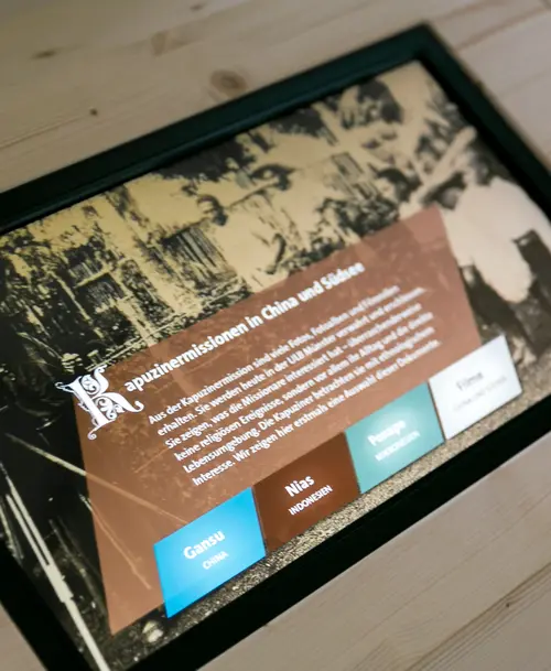 Interaktives Display in der Ausstellung mit Informationen zu Kapuzinermissionen in China und Südostasien, darunter eine historische Fotografie und Auswahlbuttons für verschiedene Regionen.