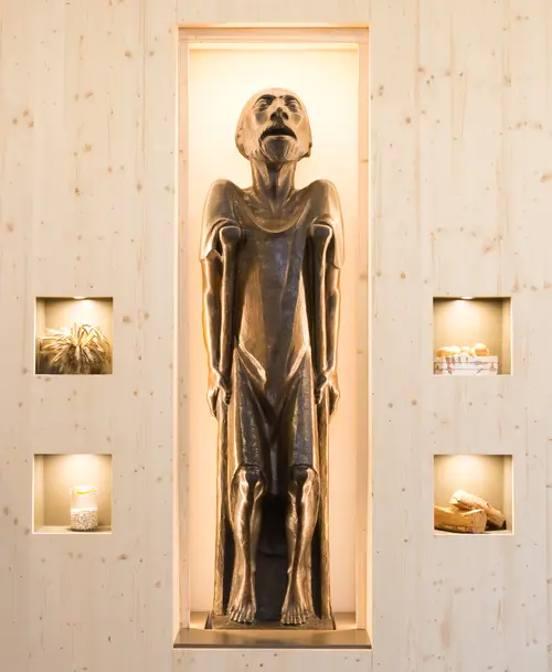 Beleuchtete Nische mit einer eindrucksvollen Skulptur eines ausgemergelten, aufblickenden Mannes. Daneben vier kleine, beleuchtete Fächer mit verschiedenen Ausstellungsobjekten.