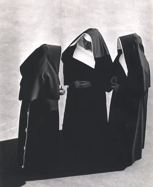 Schwarz-Weiß-Fotografie von drei Nonnen in traditionellen Ordenstrachten, die in einem Kreis stehen und sich unterhalten.