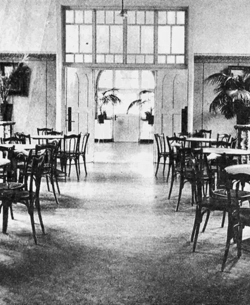Schwarz-Weiß-Fotografie eines historischen Cafés oder Speisesaals mit Holztischen, Stühlen und großen Pflanzen, im Hintergrund doppelte Glastüren mit Sprossenfenstern.
