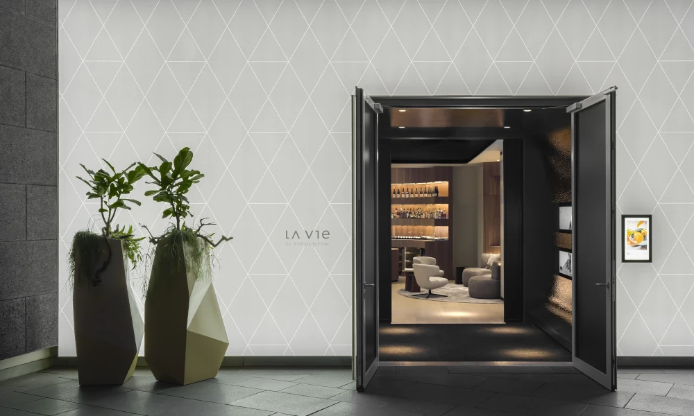 Hauseingang von LA VIE by Thomas Bühner in Düsseldorf mit offener Tür, Designer-Pflanzgefäßen und modernem Interieur.