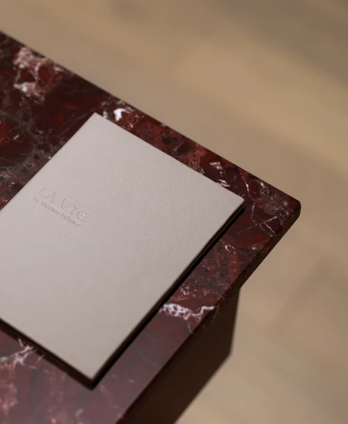 Beige Speisekarte von LA VIE by Thomas Bühner auf edlem roten Marmortisch – minimalistisches Design mit geprägtem Logo.