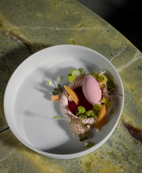 Kunstvoll angerichtetes Dessert im LA VIE by Thomas Bühner auf grünem Natursteintisch – mit Sorbet, Mini-Erdbeeren und Kräutern.