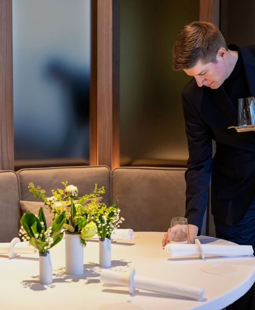 Servicekraft im LA VIE by Thomas Bühner beim Eindecken eines elegant dekorierten Tisches mit weißen Blumenarrangements.