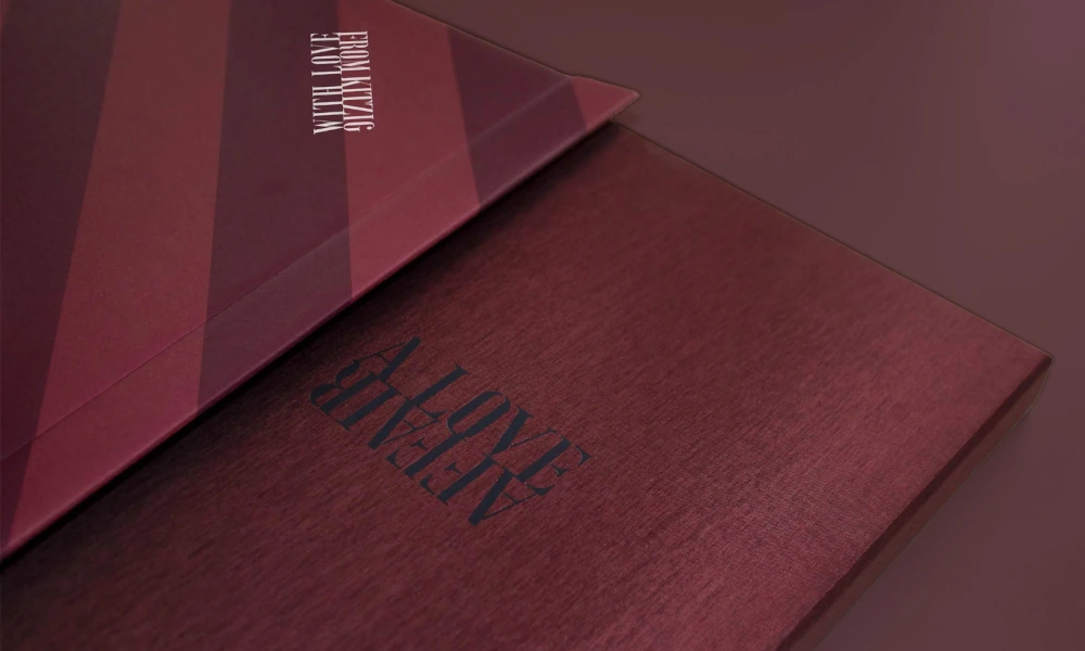 Zwei rote Bücher mit geprägtem Schriftzug „A LOVE AFFAIR“, eines teilweise von einer diagonalen Hülle mit Streifenmuster bedeckt.