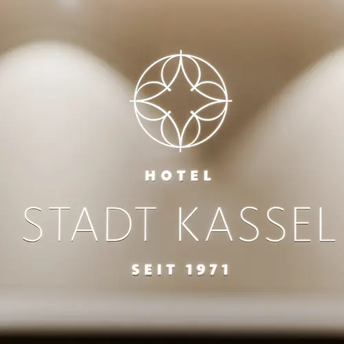 Elegantes Wandlogo des "HOTEL STADT KASSEL SEIT 1971" mit stilisiertem Kreisornament, dezent beleuchtet auf einer beigen Oberfläche.