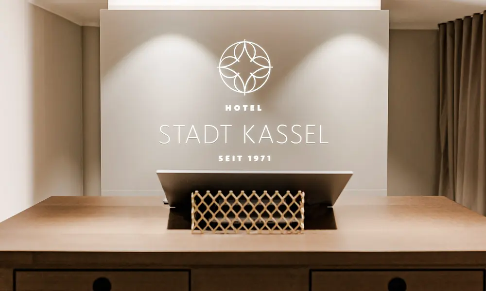 Moderner Empfangsbereich des „Hotel Stadt Kassel“ mit stilvollem Branding und dezent beleuchtetem Logo an der Wand.