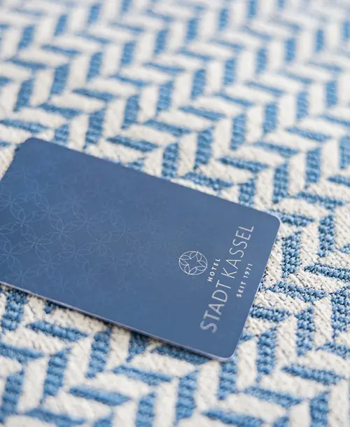 Elegante Zimmerkarte des „Hotel Stadt Kassel“ in Blau mit dezentem Muster, platziert auf strukturiertem Stoff in Blau-Weiß.