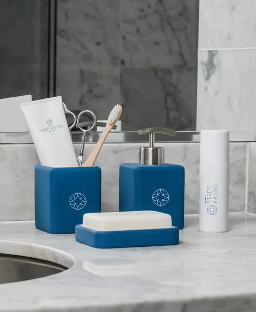 Elegante Hotel-Pflegeprodukte des „Hotel Stadt Kassel“ in blauen Spendern mit Logo, arrangiert auf einem Marmorwaschtisch.