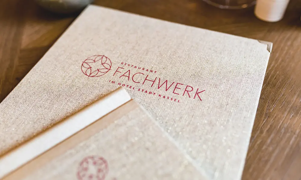 Hochwertige Speisekarte des Restaurants „Fachwerk“ im „Hotel Stadt Kassel“ mit elegantem Leineneinband und rotem Logoaufdruck.