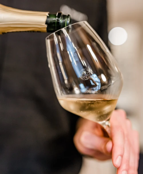 Eingeschenkter Weißwein in einem Glas mit „Hotel Stadt Kassel“ Logo, gehalten von einer Hand in stilvoller Atmosphäre.