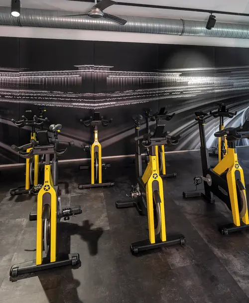 Indoor-Cycling-Bereich im Fitnessstudio mit modernen gelb-schwarzen Spinning-Bikes vor einer stilisierten Wandgrafik.