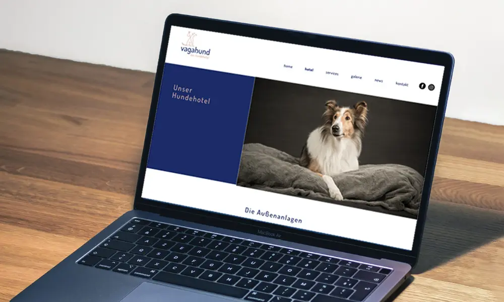 Laptop auf einem Holztisch mit geöffneter Website des Hundehotels „Vagabund“, die ein Hundebild und Navigationselemente zeigt.