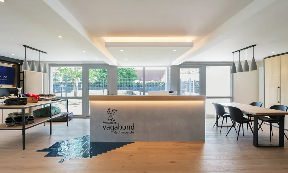 Moderner Empfangsbereich des Hundehotels „Vagabund“ mit beleuchtetem Tresen, Sitzbereich und bodentiefen Fenstern.