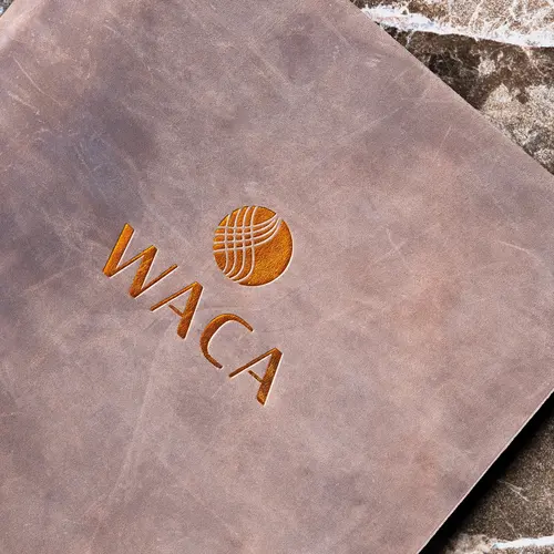 Hellbraune Ledermappe mit eingeprägtem Logo und Schriftzug "WACA", auf einer Marmoroberfläche liegend.