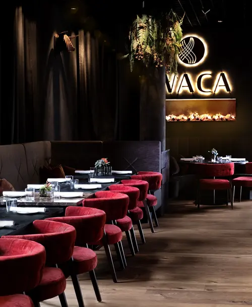 Stilvoller Restaurantbereich von 'WACA' mit roten Samtstühlen, dunklem Interieur, hängenden Pflanzen und beleuchtetem Logo.