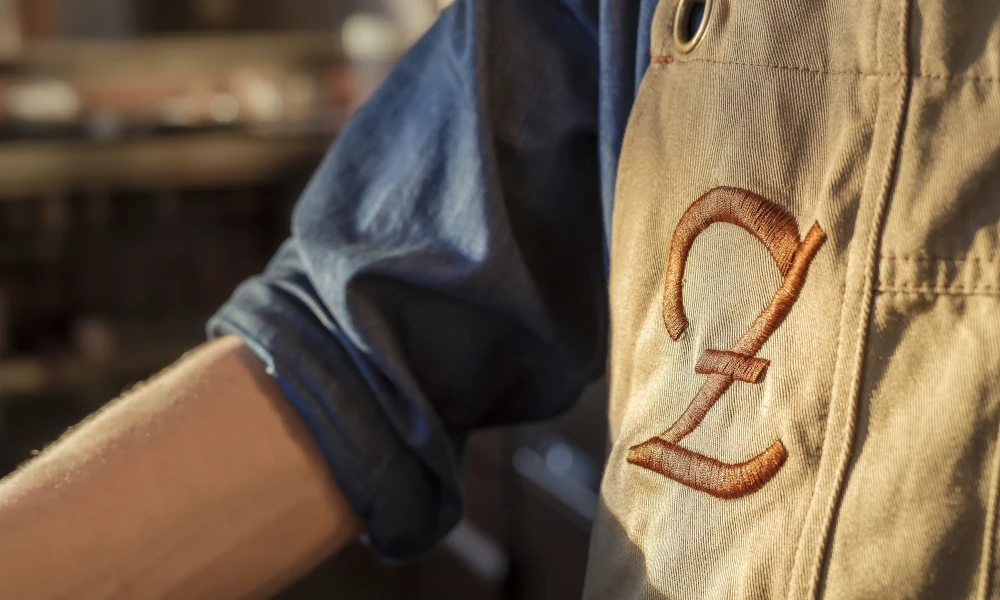 Nahaufnahme einer beigen Wirtsschürze mit gesticktem Zenz-Logo – traditionelles Handwerk trifft modernes Gastronomiedesign im Zenz Wirtshaus in Mainz.        ChatGPT fragen